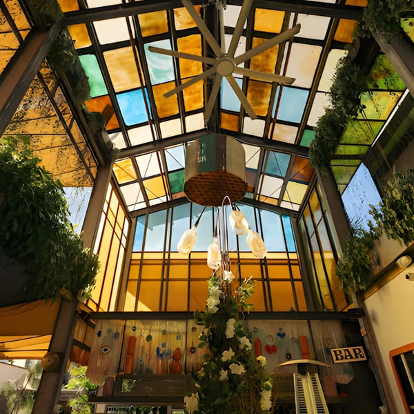 Colorful stained-glass ceiling with a large fan, hanging lights, and lush greenery in Oliva by El Turco.