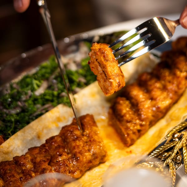 Hands cutting a piece of Mediterranean kebab from a skewer with a knife and fork.
