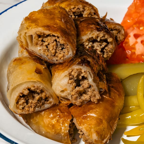 Crispy golden borek rolls filled with ground meat, served with sliced tomatoes and pickled peppers.