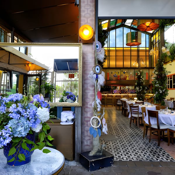 A Mediterranean restaurant interior with blue floral arrangements, a mirror, and set tables with white tablecloths.