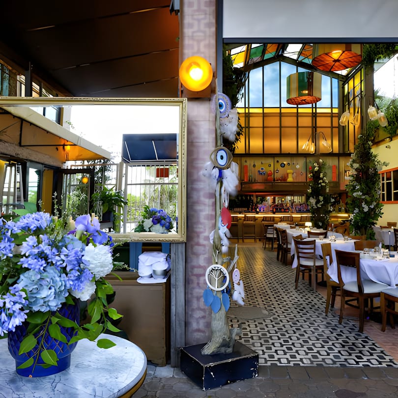 A Mediterranean restaurant interior with blue floral arrangements, a mirror, and set tables with white tablecloths.