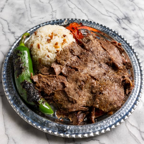 Doner kebab with rice, grilled green pepper, and red pepper on a silver platter.