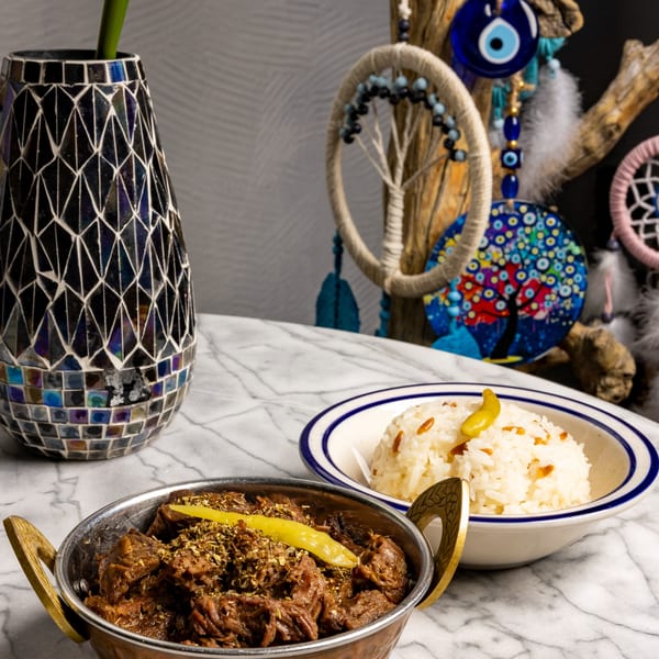 Mediterranean braised meat with herbs and a side of rice, served on a marble table.